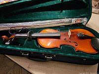 Full view of Pearl River violin inside green velvet-lined case with bow and compartment showing.