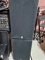 Front view of one speaker showing black fabric grille and shape