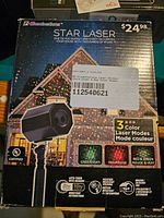 Front of the product box showing the 'Star Laser' device and highlighting features: 3 color laser modes including green, red, and combined red & green, UL certification, auto-timer, weather resistance, and indoor/outdoor use.