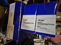 Two Brother TN780 black toner cartridges and one larger box visible, detailed packaging info. Boxes are blue and white, cartridges labeled black toner for Brother printers.