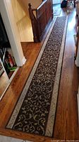 View of the acrylic runner carpet laid on hardwood floor showing its floral vine pattern and borders.