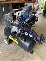 Side angle showing the full air compressor unit with blue coiled hose and air pressure gauges.