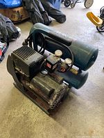 Front side view of Makita air compressor showing cylindrical tank, compressor unit, and attached pressure gauges, with visible wear and dust.