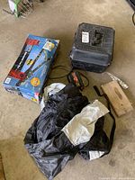 Photo showing a folded black and grey motorcycle cover, Simoniz polisher, Motomaster 400W power inverter hard plastic case, Reese tow bar box on the floor