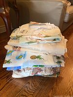 Stack of assorted linens showing multiple folded pieces including varied prints like pineapples and florals