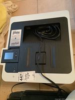 Top front angled view of Brother HL-L3270CDW color laser printer with power cord placed on top, label showing printer information and toner cartridges included.