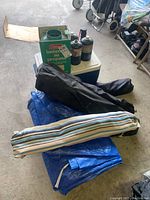 Overall assortment of camping items including camping chairs in bags, hammock in bag, blue tarp, cooler, propane tanks, and boxed propane lantern.