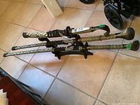 Three ceremonial swords horizontally arranged on a tile floor, showing snake skin patterned scabbards with black cord wrapped handles and textured pommels, resting on a black wooden display stand.
