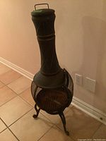 Full view of the black metal chimenea fireplace standing on tile floor, showing tall chimney and round fire chamber with mesh sides and door.