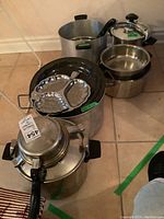 Overall view of pressure cookers, stock pots, and enamelware divided server showing condition and items together.