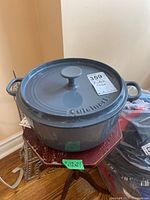 Gray Cuisinart cast iron Dutch oven on wooden stand, top view showing lid with brand embossing and price tag.