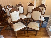Front view of six dining chairs grouped together on a wood floor. Two captain armchairs with upholstered seats and backs and four matching armless chairs with similar upholstery.