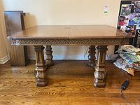 Full front view of the wooden dining table showing carved apron and pedestal legs.