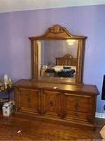 Front view of wood dresser with six drawers and central door beneath large mirror with carved wooden frame and decorative top.