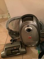 Front view of Hoover WindTunnel vacuum, showing the canister body, hose, and vacuum attachment head on tiled floor.