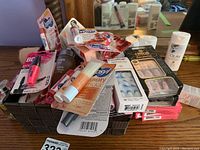 Top view of basket filled with assorted lip balms, lip glosses, body wash, perfume, mascara and other small makeup items.