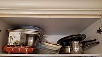 Shelf of kitchen cookware including metal pans, ceramic dishes, and trays.