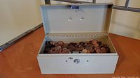 Open metal money box showing a large quantity of U.S. pennies inside.