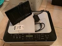 Canon Pixma MX320 all-in-one scanner printer with numeric keypad and LCD screen. Power adapter and a digital photo frame resting on top.