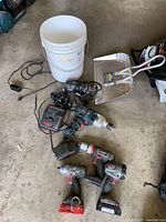 Photo of the entire lot including drills, router, battery charger, dust pan, and bucket on concrete floor.
