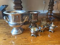 Photo showing all silver plated dishes including ice buckets, sugar bowl, creamer, goblets, tray, and small pitcher on wood floor.