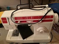 View of the white and red Singer sewing machine showing stitch function options and control dials on the body.