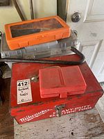 Stack of toolboxes including a red Milwaukee metal toolbox with a crowbar on top and a red plastic case, positioned by a door.