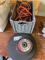 Plastic bin containing orange extension cords with grinding wheels stacked nearby on the wooden surface.