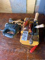 Photo showing Bosch electric corded drill with orange power cord, hand drill with wooden handles, two screwdrivers atop a yellow toolbox.