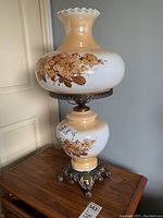 Side view of one lamp showing beige and white ceramic body with floral decals and ruffled top shade.