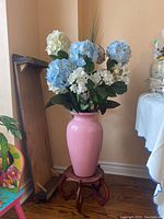 Full view of pink ceramic vase on wooden plant stand with faux blue and white hydrangea flowers in arrangement