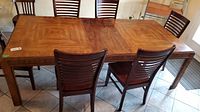 Full frontal view of the wooden dining table with 6 chairs around it. Table has a medium brown wood finish and visible wood grain.