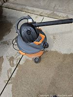 Ridgid wet/dry vacuum and leaf blower combo unit in orange and gray with hose attachment and wheels.