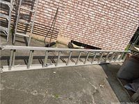 Full side view of the aluminum extension ladder showing length and rung structure on pavement area.