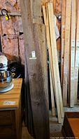 Stack of reclaimed barn wood slabs leaning against wall, showing variety in size and rough texture of wood including knots and cracks.