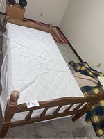 Full view of the single wooden bed frame with mattress showing turned posts on footboard and vertical slats