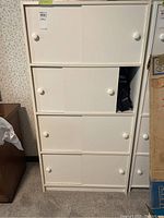 Front view of white pressboard cabinet showing four shelves with two sliding doors per shelf and round white knobs on each door.