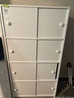 Front view of white pressboard cabinet showing four shelves with two sliding doors each, all doors have round white knobs.