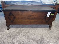Front view of a dark wood cedar chest with visible scratches and decorative carved panels on the sides.