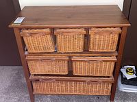Front view of the wooden cubby dresser showing three shelves with six wicker baskets arranged: three on top, two in the middle, and one at the bottom.