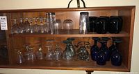 Full shelf display of assorted glassware including blue and clear glasses with some chips noted