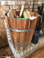 Front and side views of wooden barrel log holder filled with logs, showing metal bands and handles