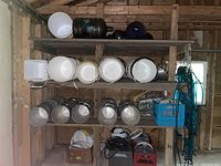 Multiple shelves showing white and black plastic buckets, galvanized steel buckets and green vinyl tubing hung on a beam.