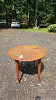 Full view of round wood side table outdoors showing table top wear and four tapered legs