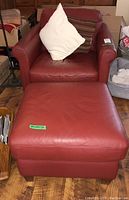 Red leather Natuzzi armchair with matching ottoman and two pillows on wooden floor, room background.