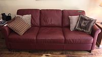 Front view of the red leather Natuzzi Editions sofa with four decorative pillows, showing overall condition and seat cushions.