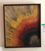 Full frontal view of the framed painting showing the abstract sunburst design with colors yellow, orange, red and black.