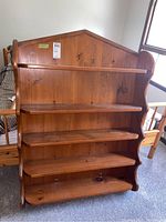 Full view of pine wall shelf showing five shelves and peaked top design with curved sides.