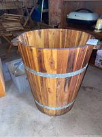 Full view of wooden barrel style plant holder showing wood slats with metal bands and one wooden handle visible.