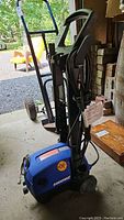 Front and side view of the blue Simoniz pressure washer on wheels, showing handle and attached hose.